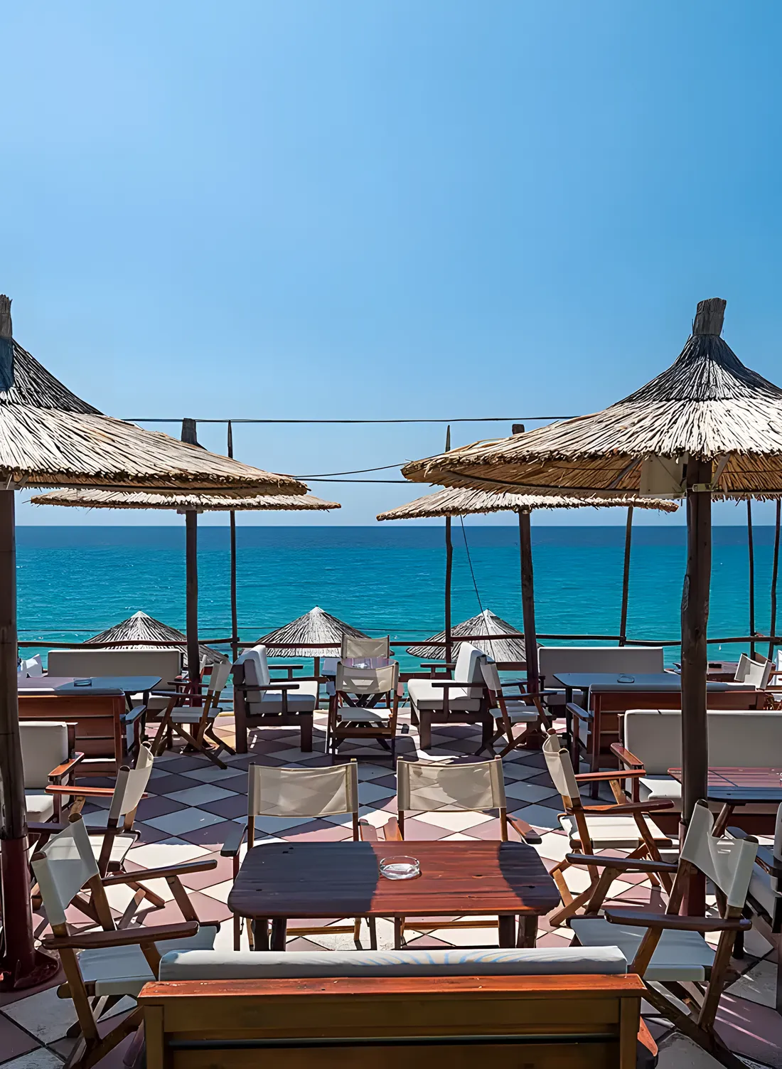 Kudu's beachfront terrace in bright morning light, straw umbrellas over the turquoise Aegean