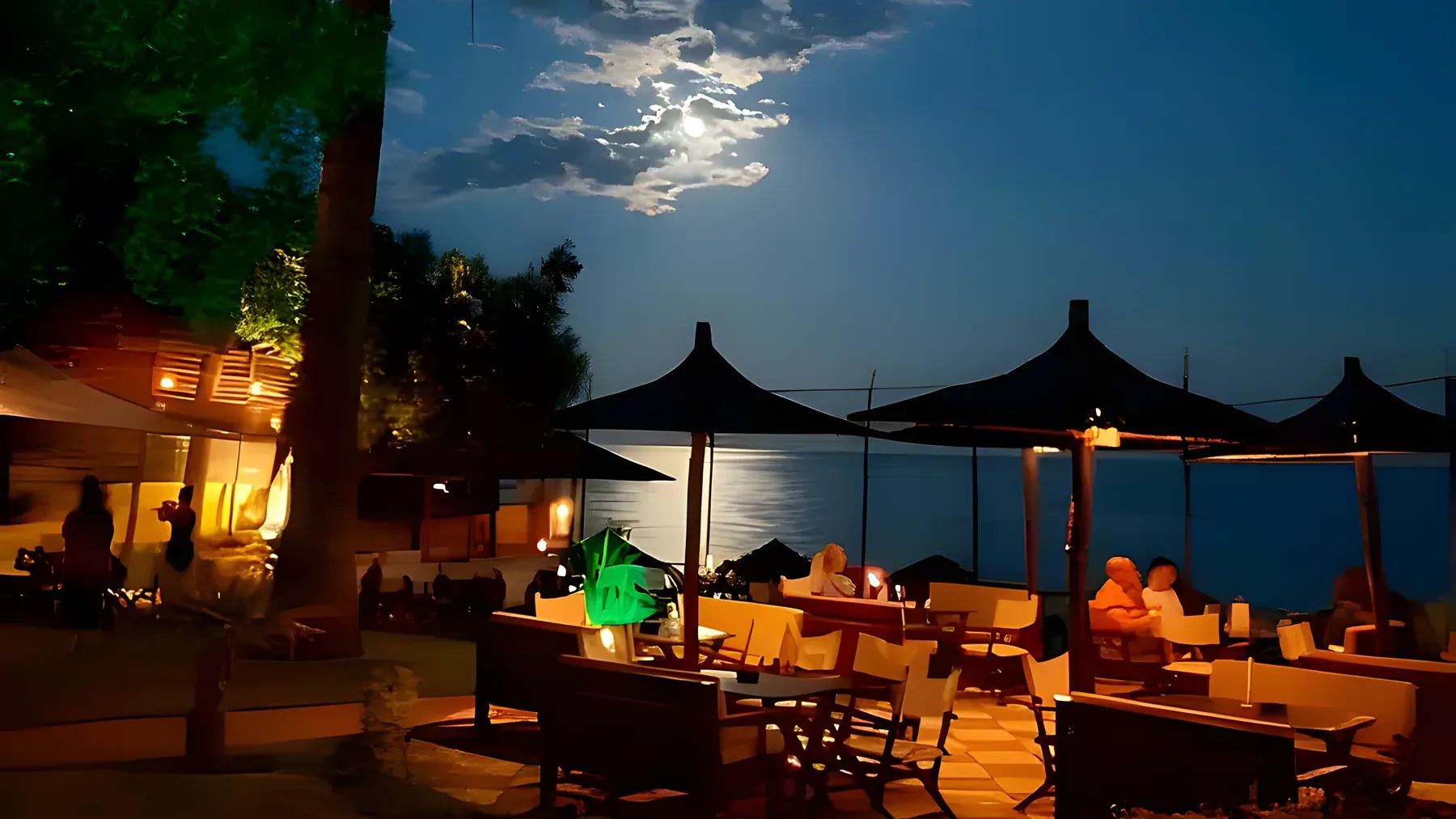 Kudu's terrace after dark, lanterns and garden lights glowing over the night sea