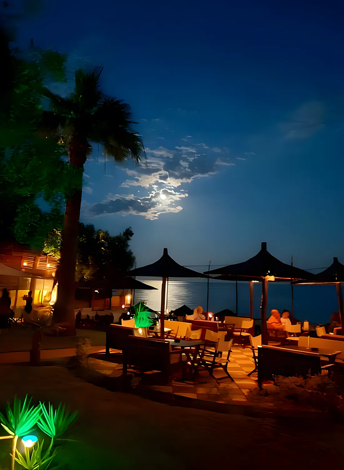 Kudu's terrace after dark, lanterns and garden lights glowing over the night sea