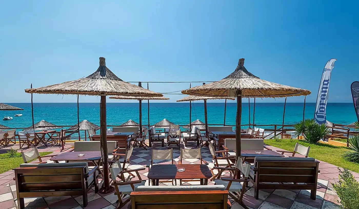 Kudu's beachfront terrace in bright morning light, straw umbrellas over the turquoise Aegean